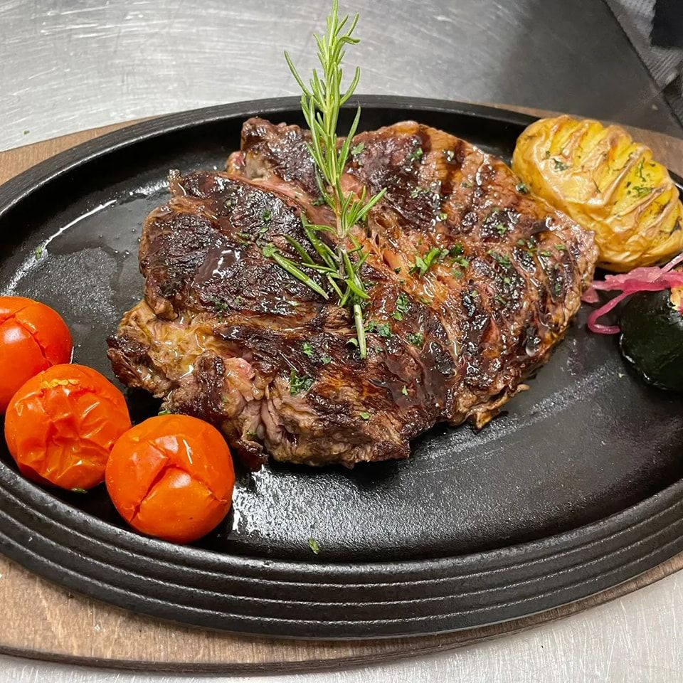 Bistecca alla griglia su un piatto nero con pomodorini ciliegino grigliati, aglio arrostito ed erbe aromatiche.