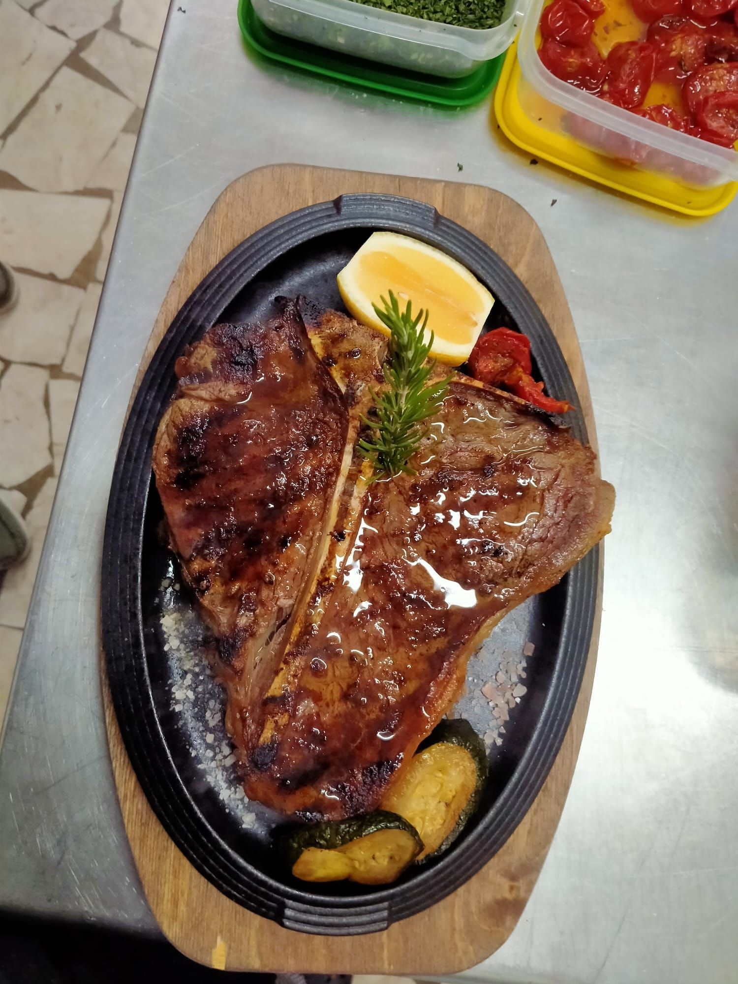 Bistecca alla griglia su un piatto sfrigolante con spicchio di limone e verdure su un tavolo