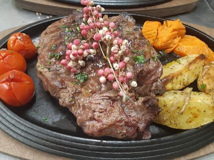 Bistecca alla griglia con verdure arrosto e contorno su un piatto nero.