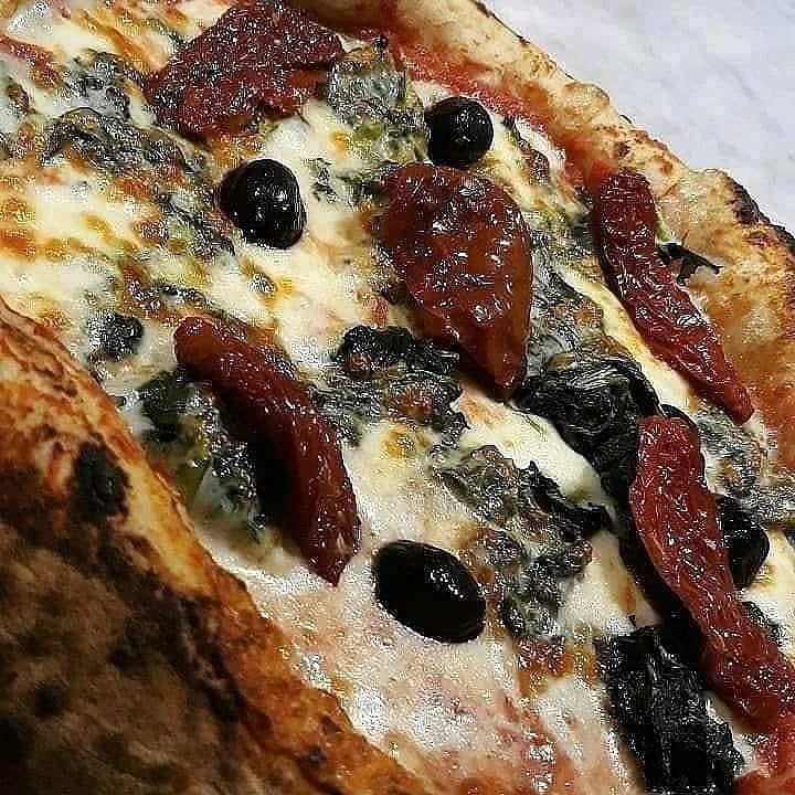 Primo piano di una pizza con formaggio fuso, olive nere e peperoni rossi arrostiti.
