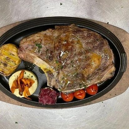 Piatto ovale con una grande bistecca alla griglia, patate arrosto, pomodorini e due piccole porzioni di contorno.