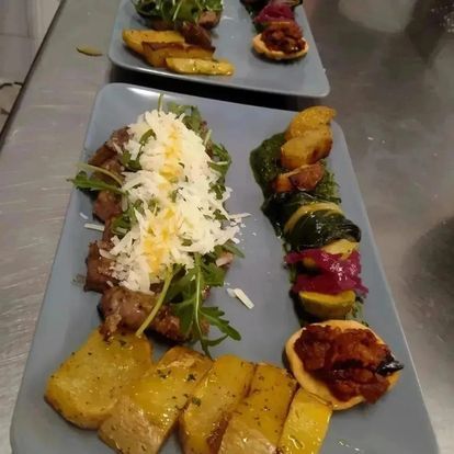 Antipasti gourmet serviti su piatti grigi, tra cui spiedini, verdure, formaggio e fette fritte, su un tavolo in acciaio inox.