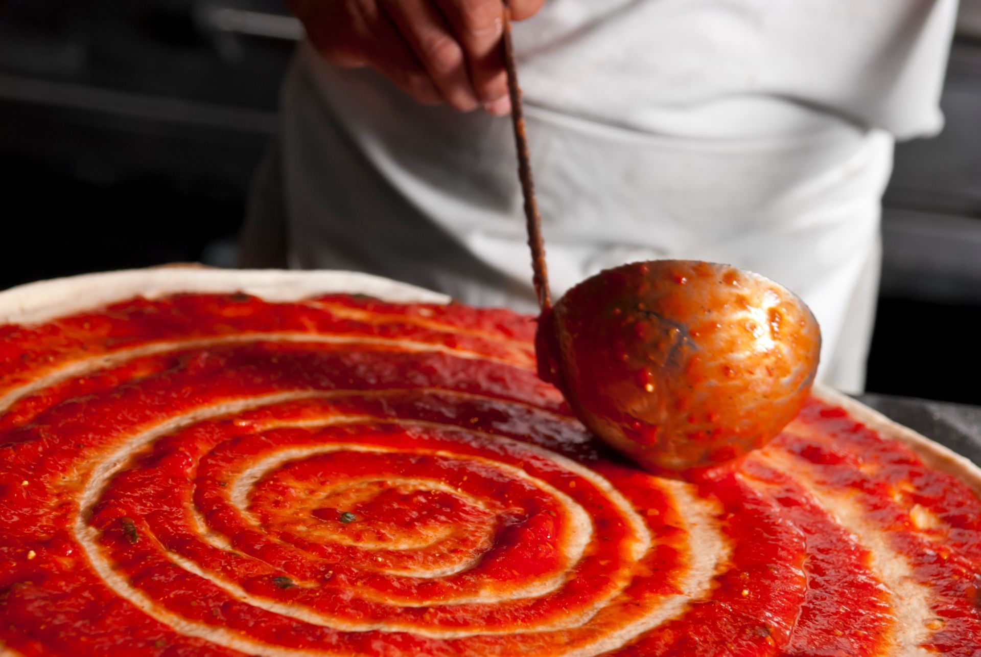 Persona che versa salsa rossa a spirale su una pizza o una focaccia.