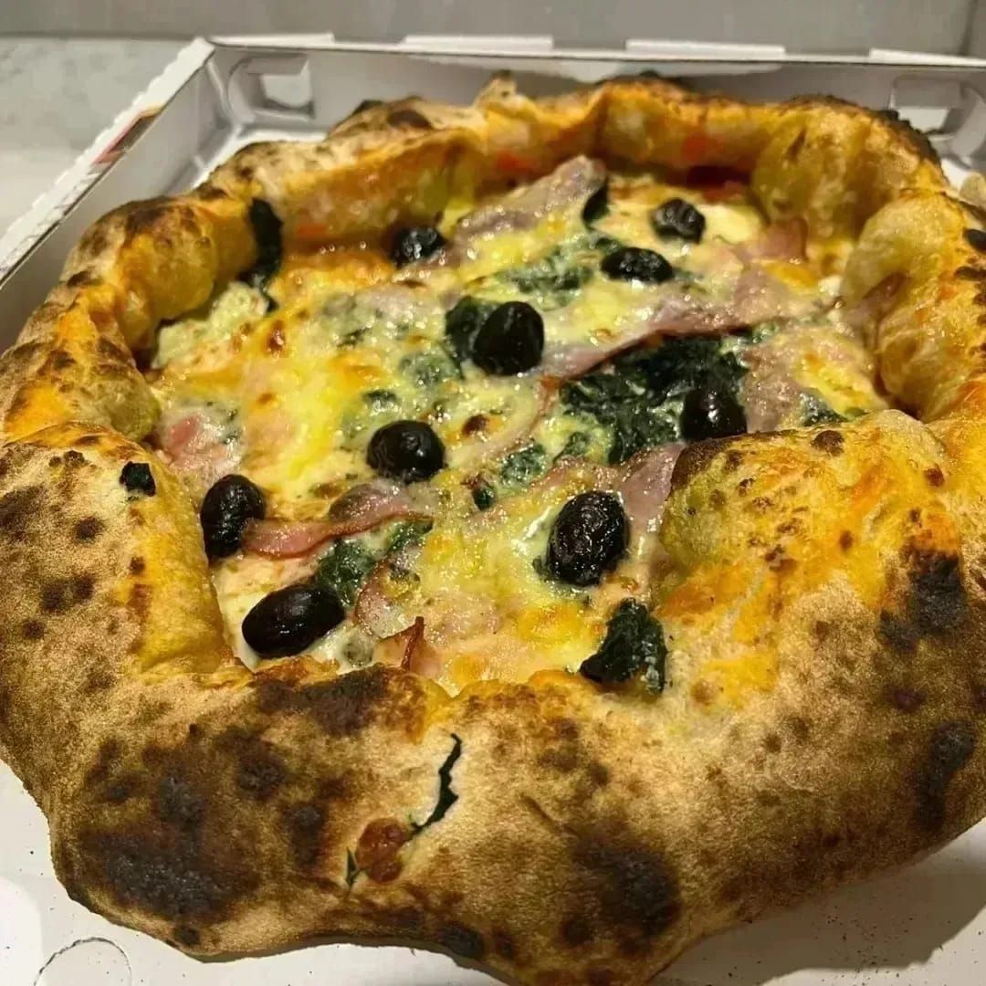 Pizza ricca di formaggio con olive nere e crosta bruciacchiata in una scatola di cartone.