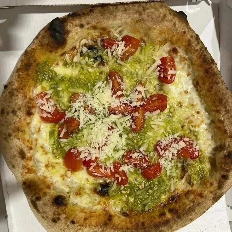 Pizza cotta nel forno a legna con pomodorini, formaggio grattugiato e salsa verde, servita su un piatto.