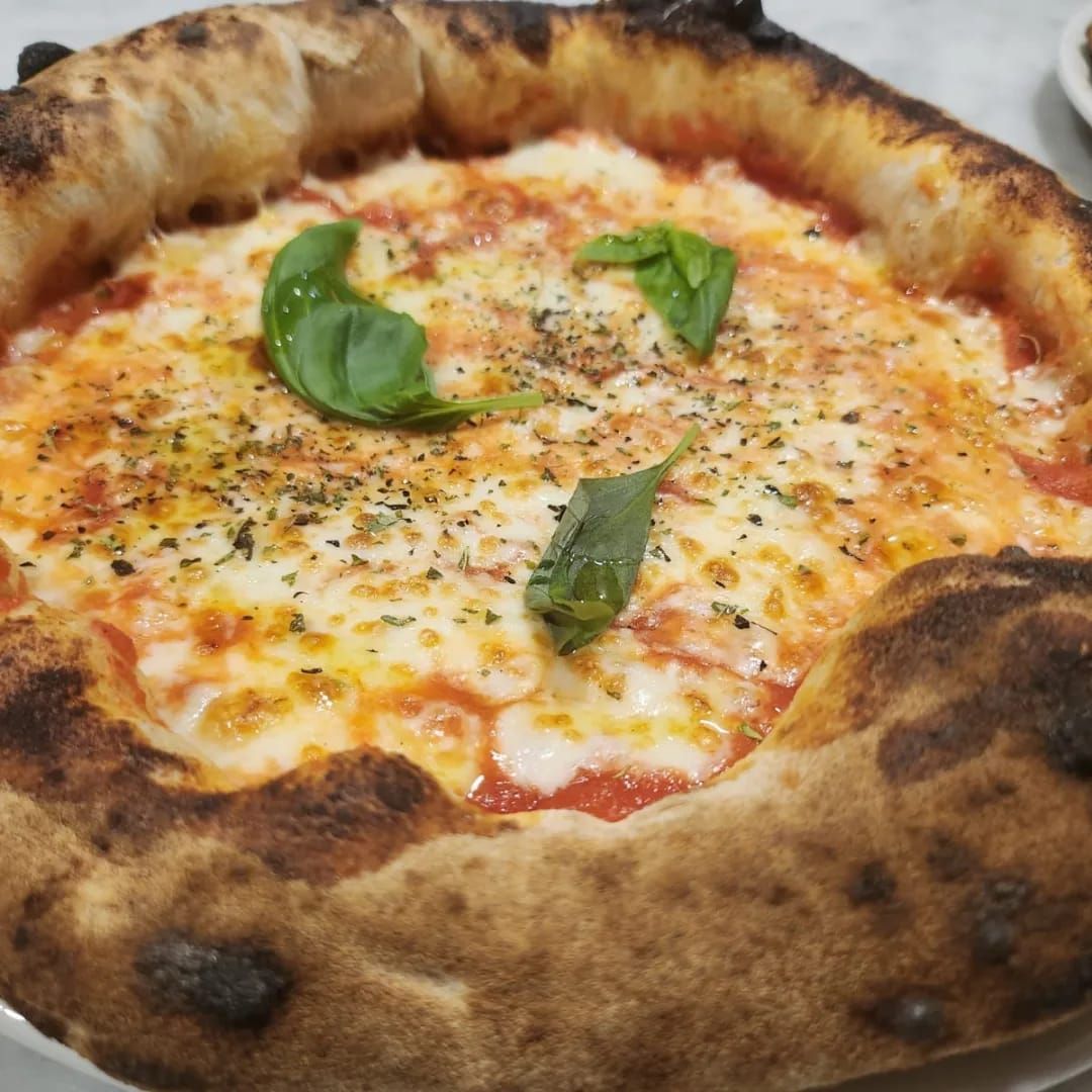 Pizza cotta nel forno a legna con formaggio fuso, foglie di basilico e crosta leggermente bruciacchiata.