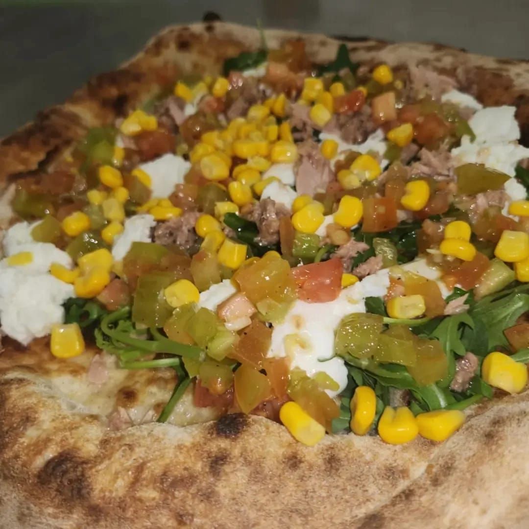 Pizza su pane piatto condita con mais, verdure a dadini, erbe aromatiche e formaggio fuso