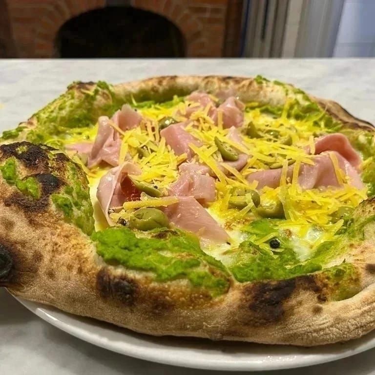 Pizza condita con prosciutto, formaggio grattugiato e salsa verde su un piatto bianco