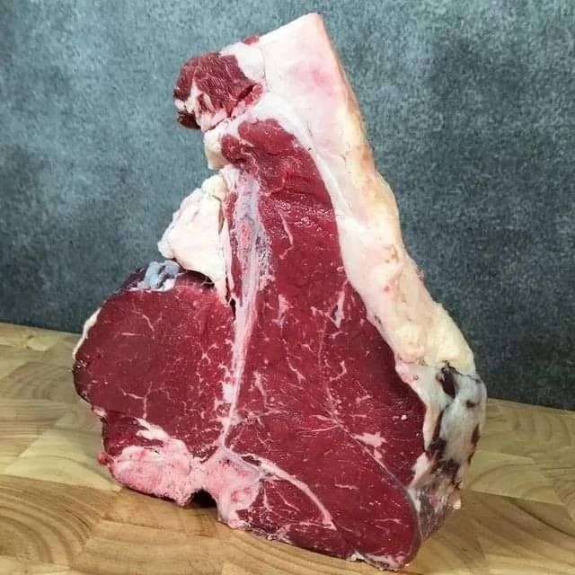 Bistecca di manzo cruda su un tagliere di legno con uno spesso strato di grasso bianco, su uno sfondo grigio.