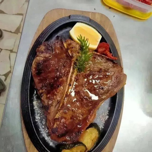 Bistecca alla griglia servita su una piastra sfrigolante con spicchi di limone e un rametto di rosmarino.