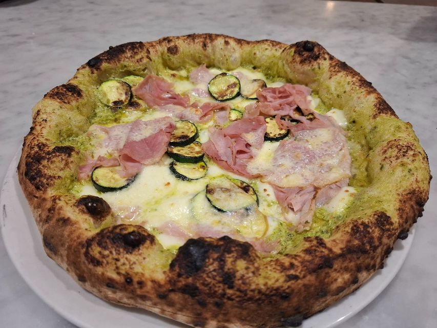 Pizza con prosciutto, zucchine a fette e formaggio fuso su un piatto bianco