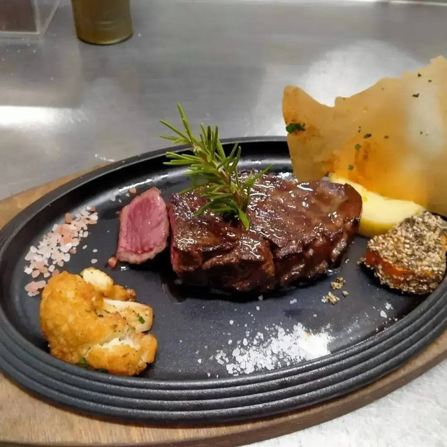 Cena a base di bistecca con carne rosa a fette, crocchette di patate, guarnizione e patatine croccanti su un piatto nero.