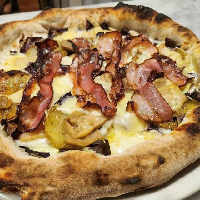 Primo piano di una pizza con pancetta e patate, formaggio fuso e crosta bruciacchiata.