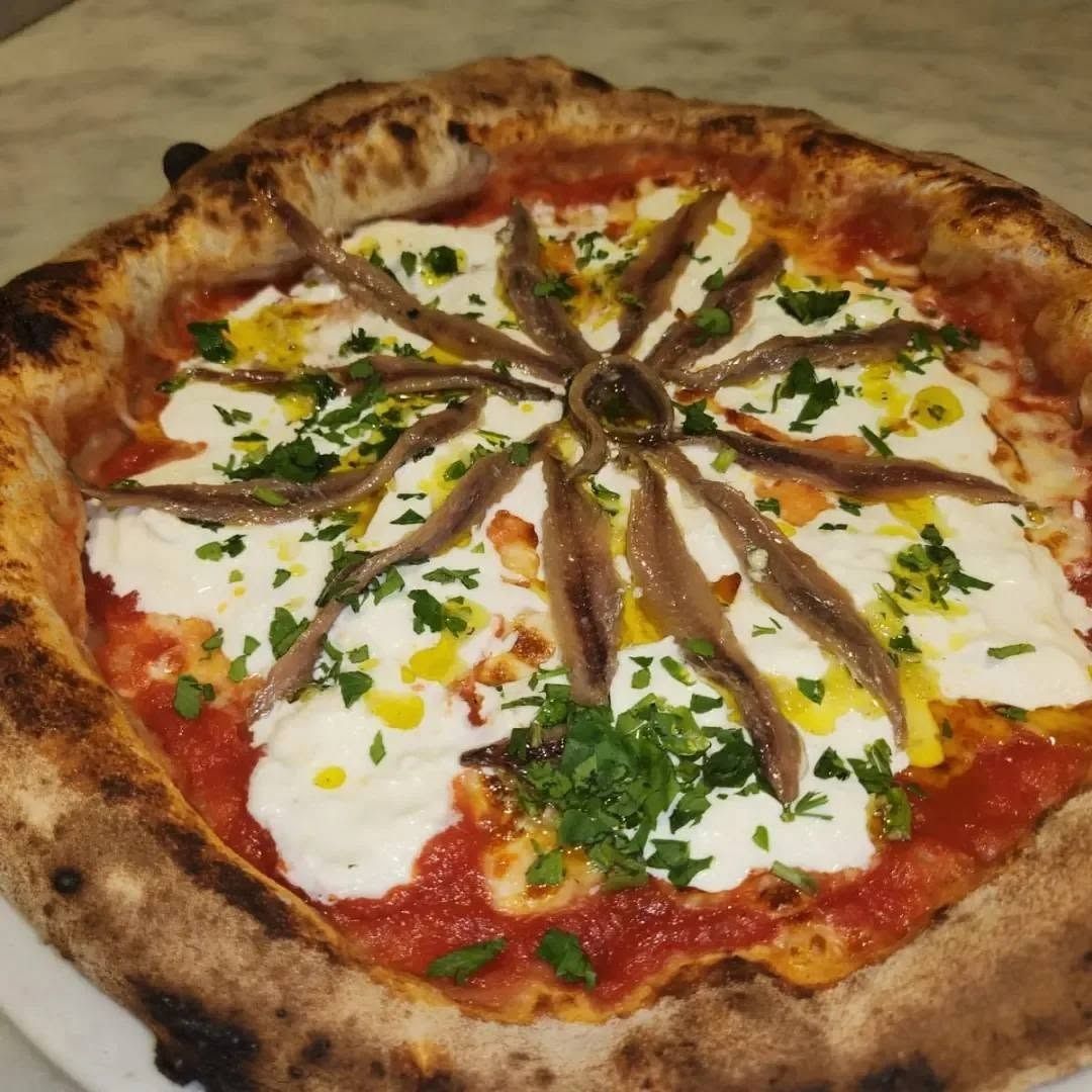 Pizza condita con acciughe, basilico, formaggio bianco e salsa di pomodoro.