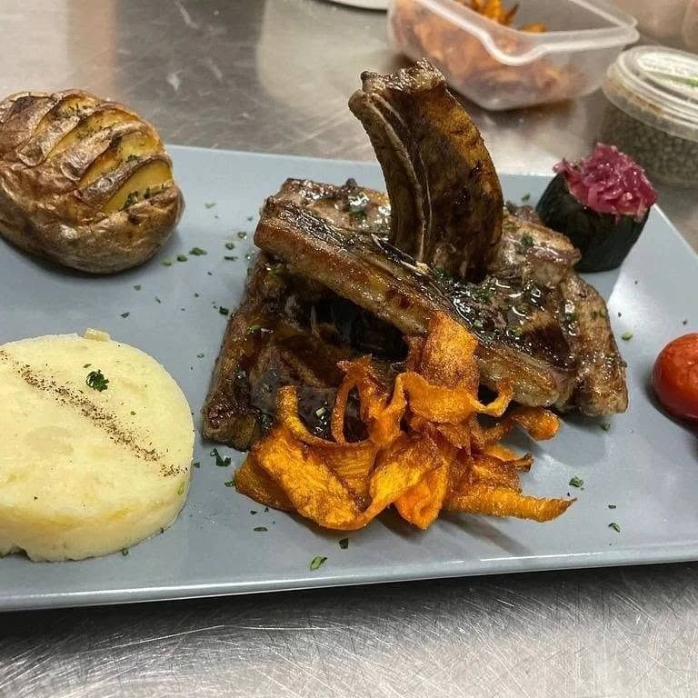 Costine di maiale alla griglia con purè di patate e verdure arrosto su un piatto grigio