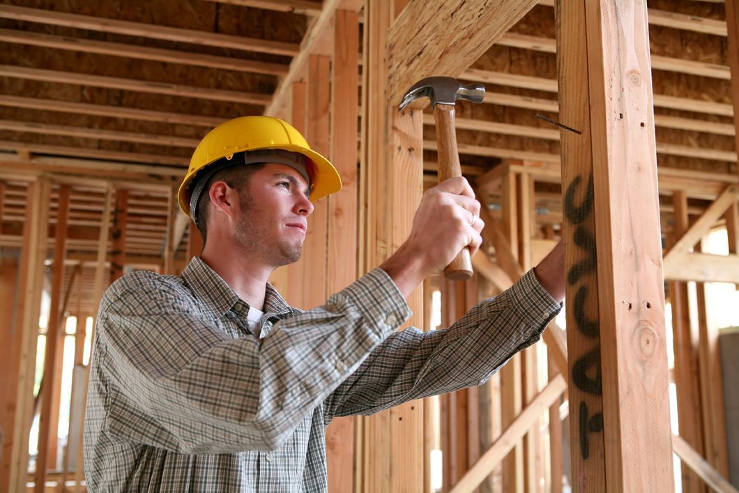 Construction worker in a yellow hard hat inspecting wooden framing inside a building under construction