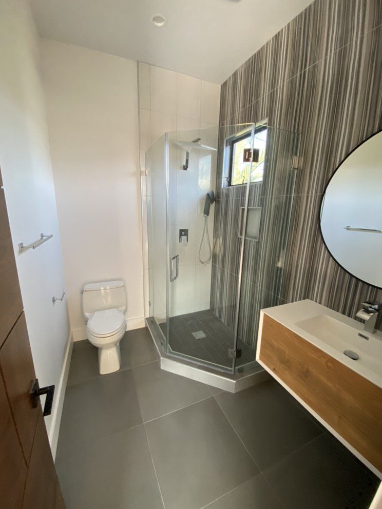 Modern bathroom with toilet, glass shower, and wood vanity with round mirror