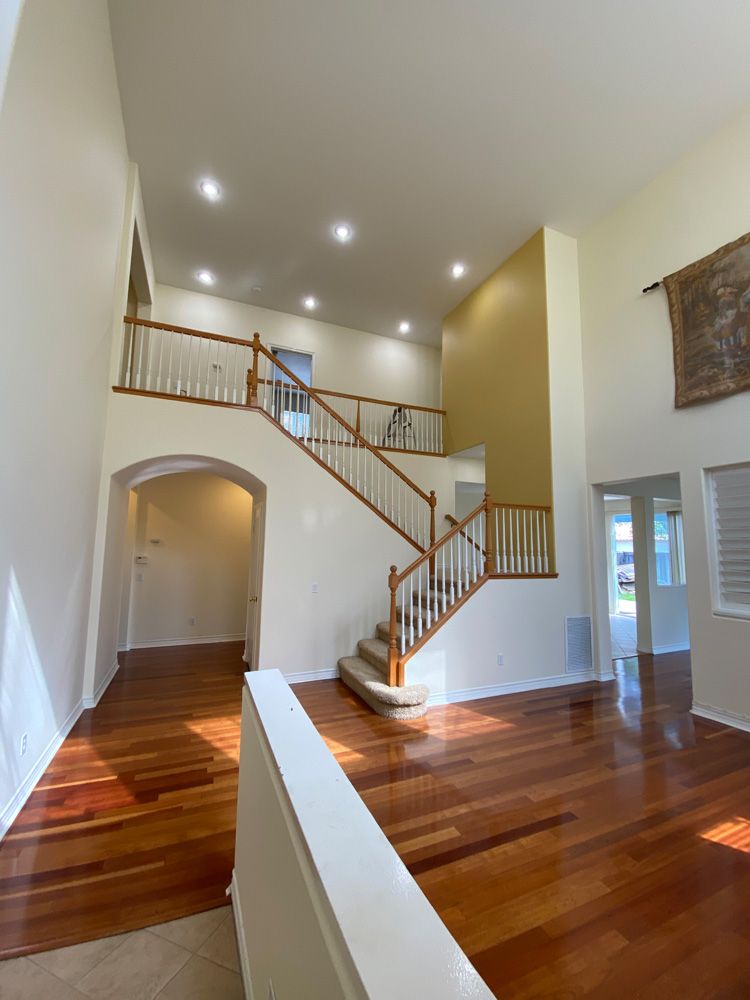 Spacious foyer with hardwood floors, staircase, arched doorway, and upper balcony railing under recessed lights