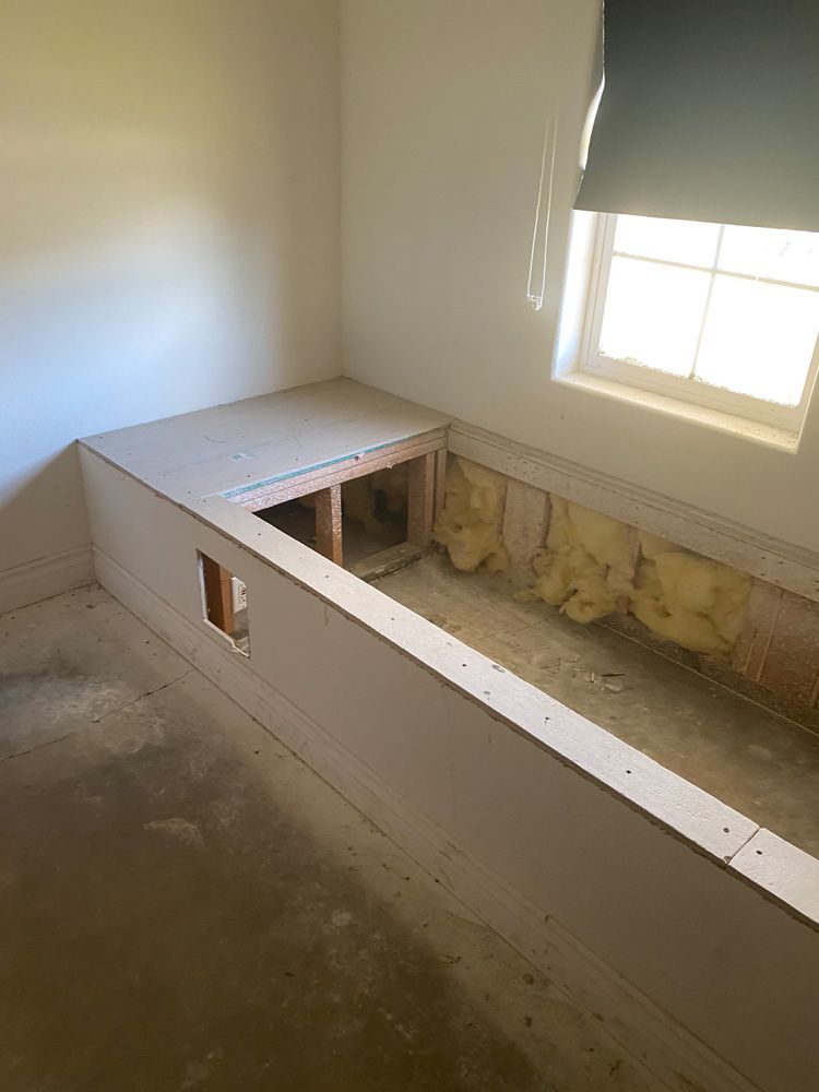 Partially built wooden platform or bed frame in an unfinished room by a window
