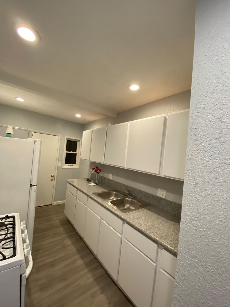 Bright white galley kitchen with cabinets, granite counters, gas stove, and recessed ceiling lights
