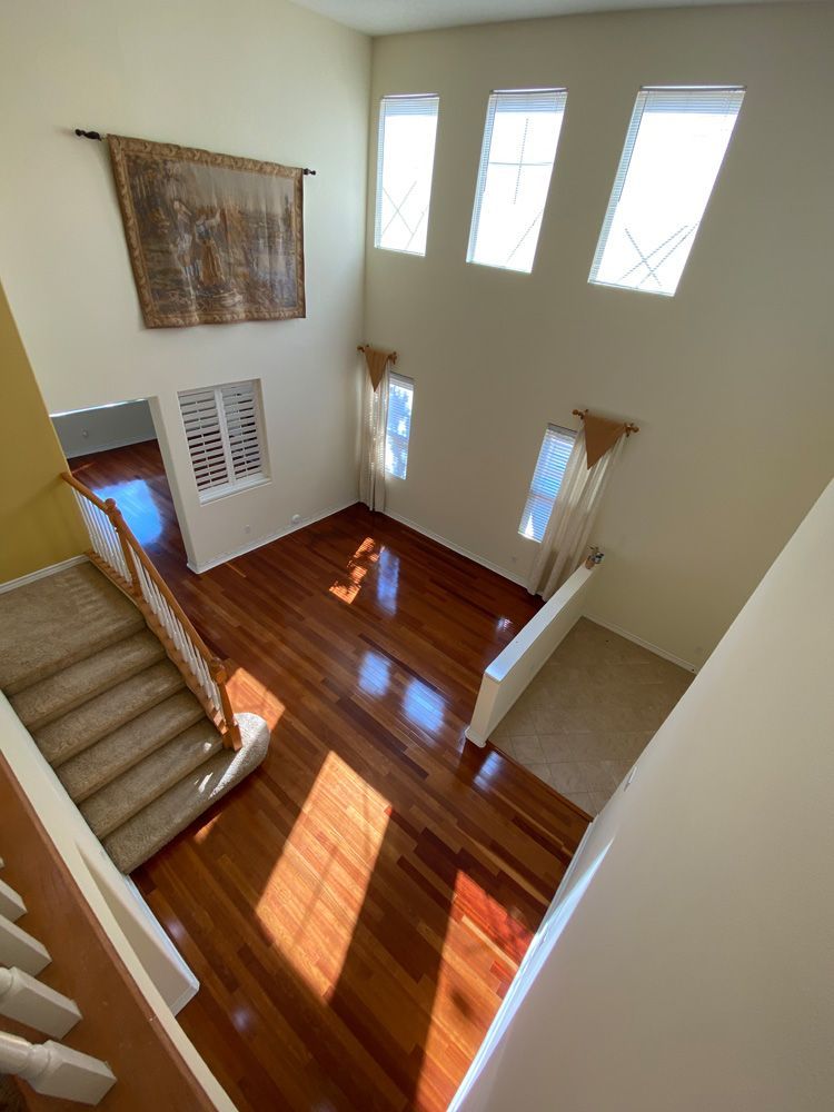 Stairwell with wood floor, beige walls, white railings, and tall windows casting sunlight.