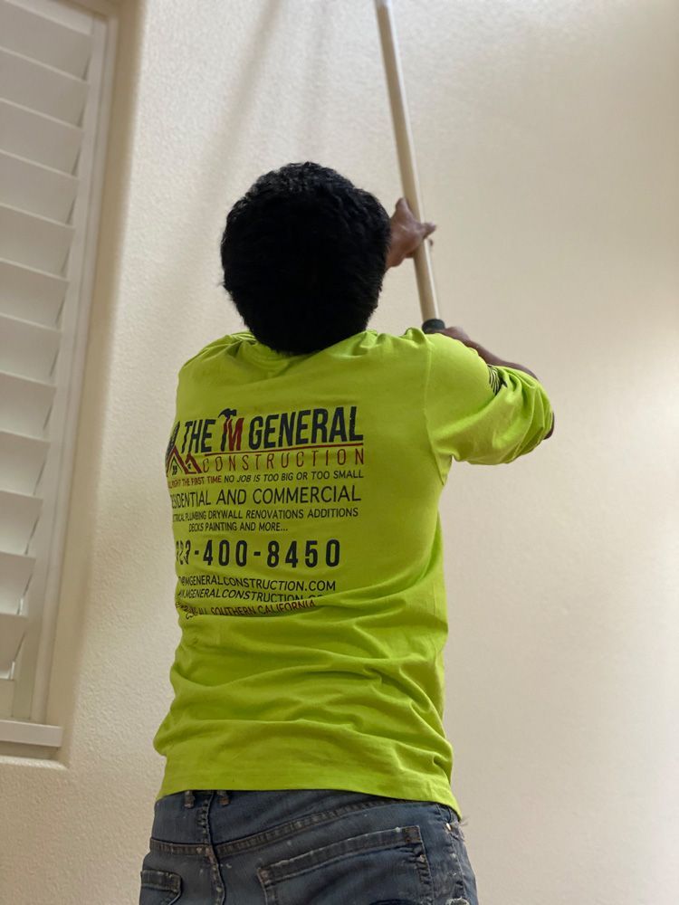 Person in a neon yellow shirt painting a ceiling with a long pole in a stairwell.