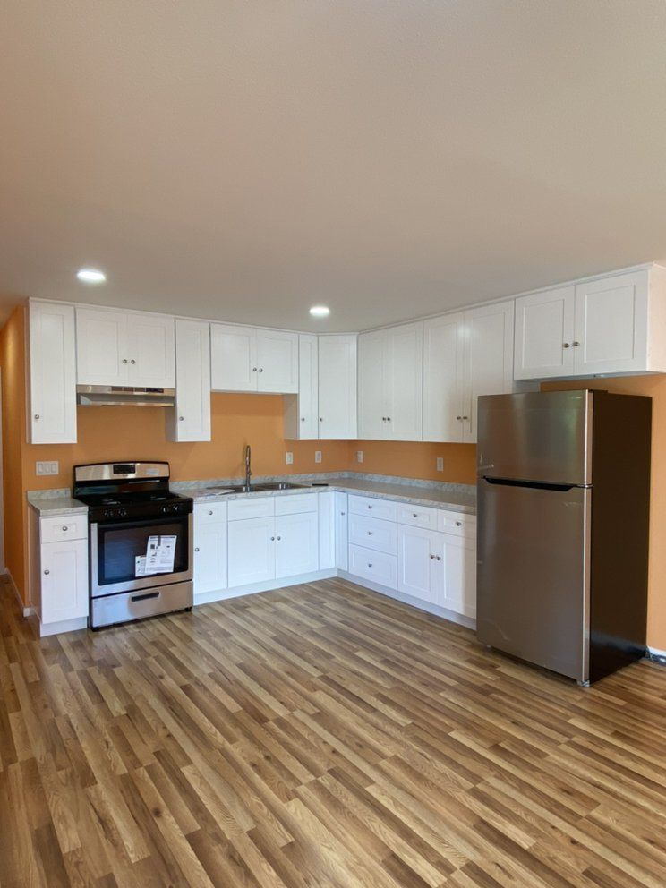 Bright kitchen with white cabinets, stainless steel fridge, gas stove, and wood-look flooring