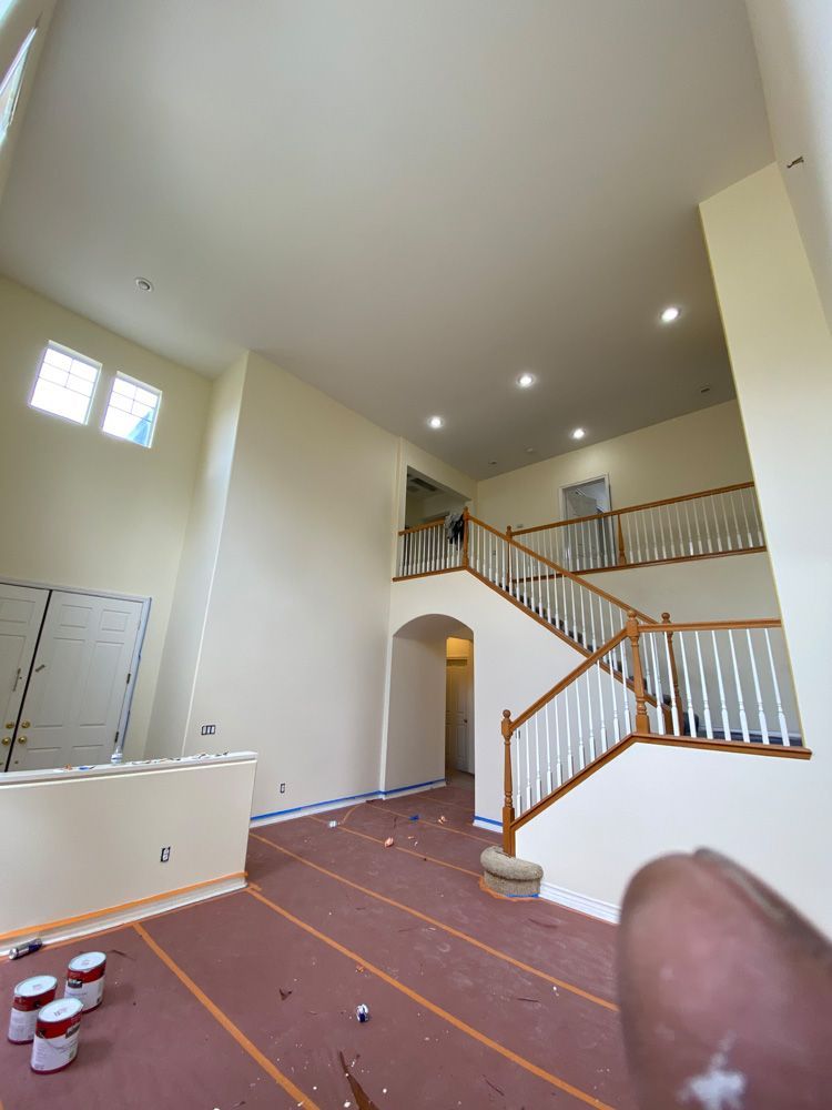 Large unfinished living room with tall ceiling, staircase, arched doorway, and paint supplies on the floor