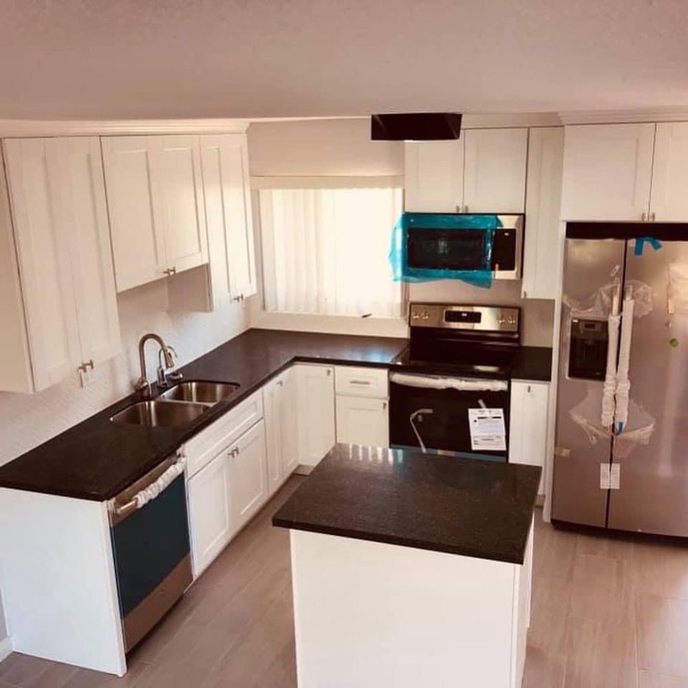 Modern white kitchen with black countertops, island, stainless fridge, and microwave over stove