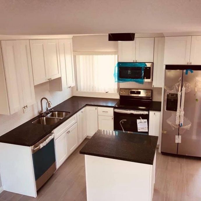 Bright white kitchen with black countertops, stainless steel appliances, and a central island