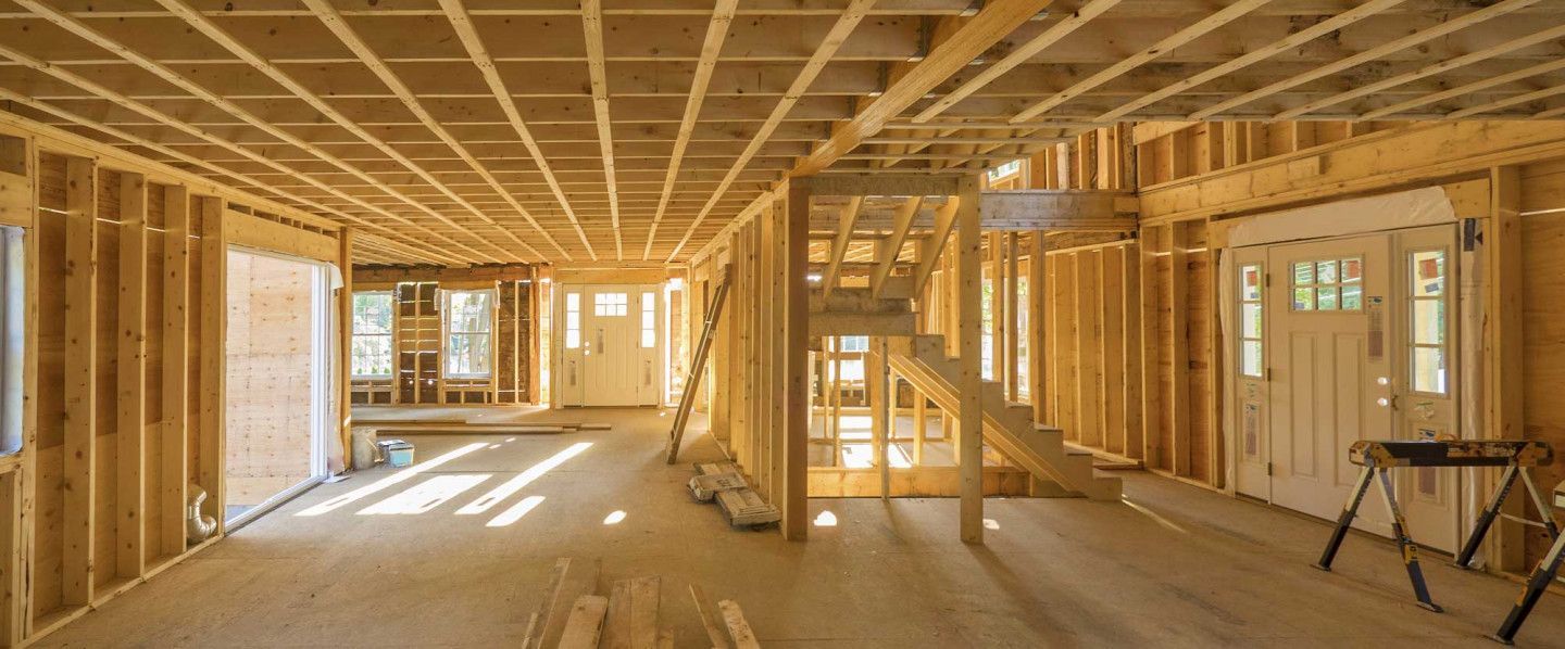 Interior of a framed house under construction, with exposed wooden walls, beams, and bright sunlight.