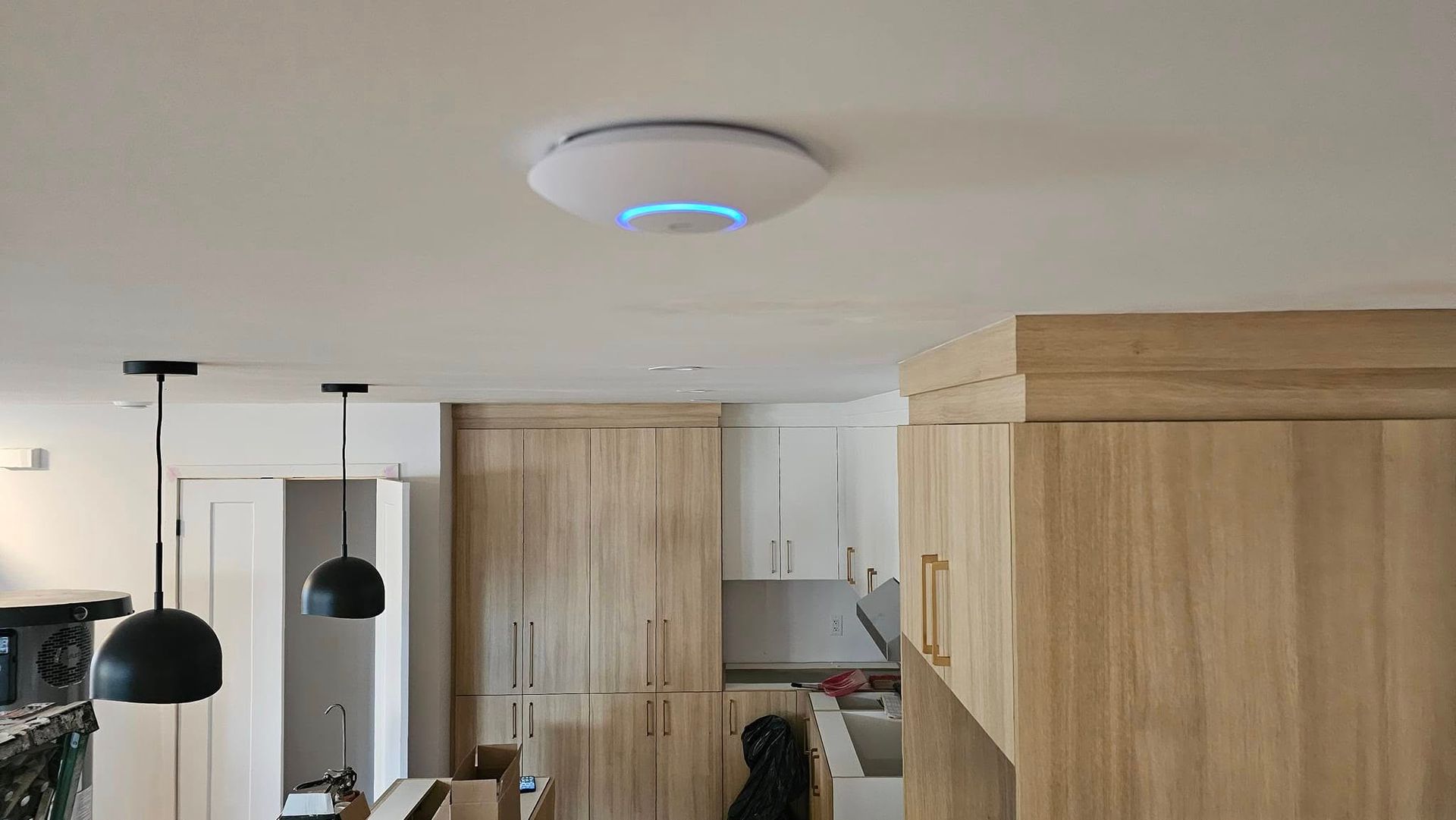Un point d'accès Wi-Fi blanc et circulaire, doté d'un anneau lumineux bleu, fixé au plafond au-dessus d'une cuisine aux placards en bois.