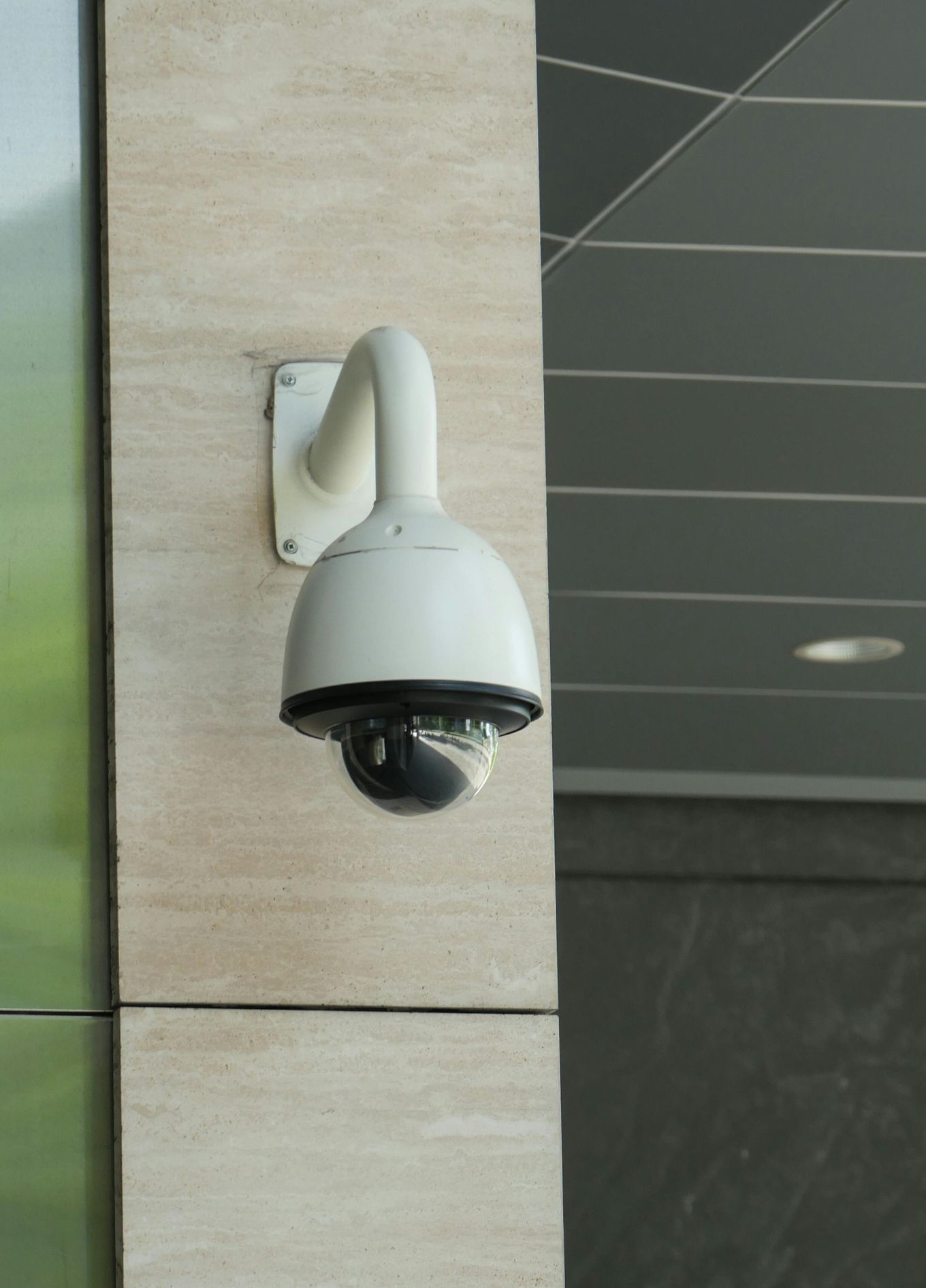 Une caméra de sécurité blanche en forme de dôme, fixée sur un mur carrelé beige.