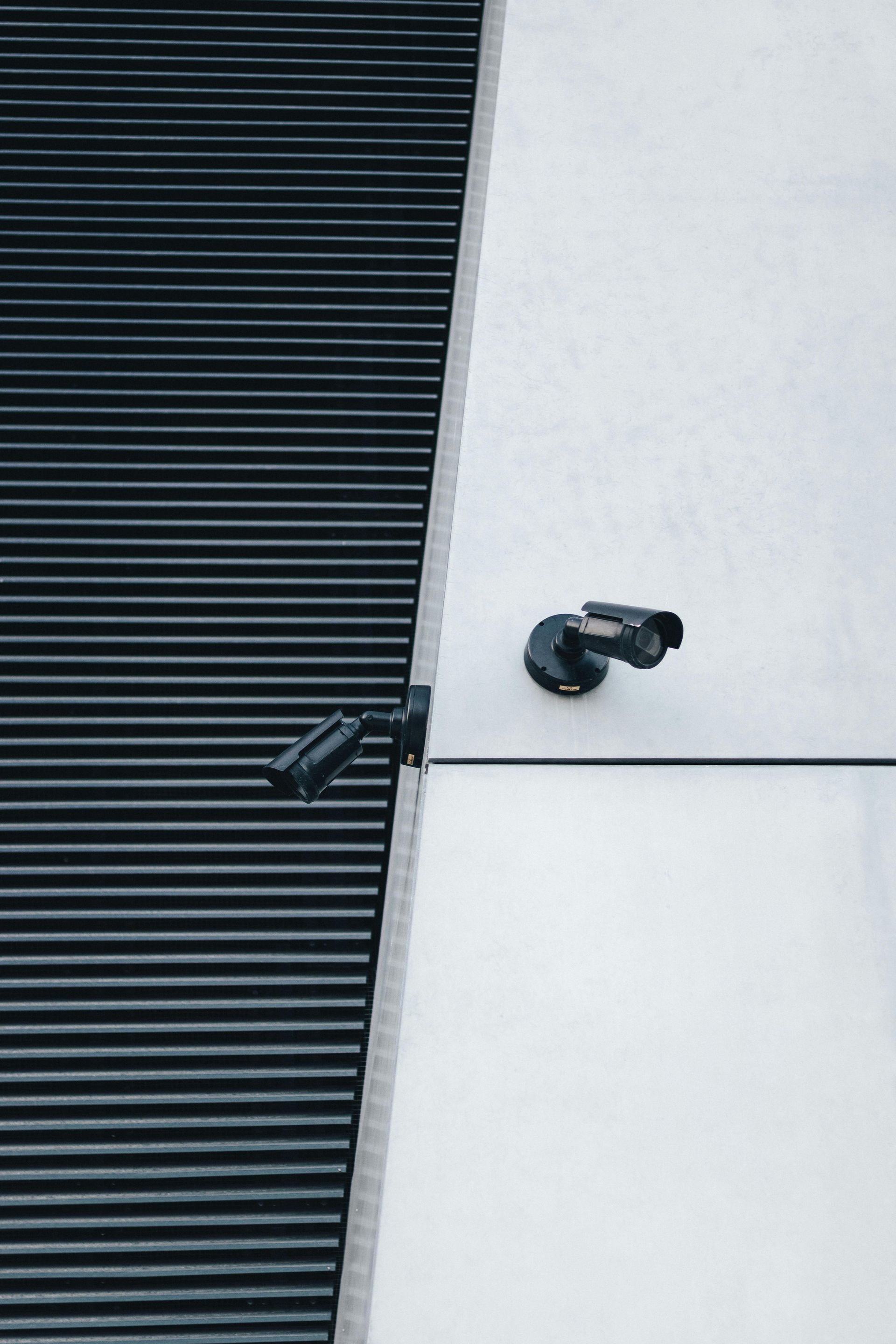 Deux caméras de sécurité noires fixées sur un mur recouvert de panneaux blancs et de bardage métallique foncé à lattes.