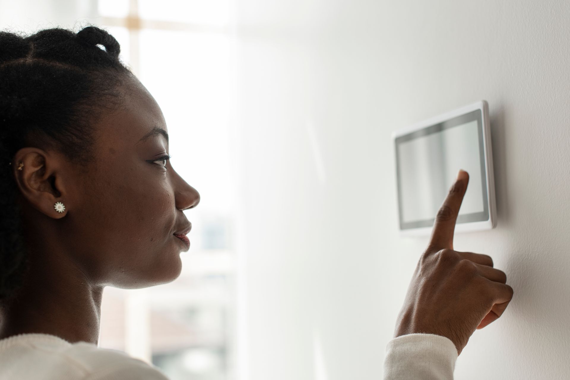 Une personne touchant un panneau de commande numérique mural pour la maison.