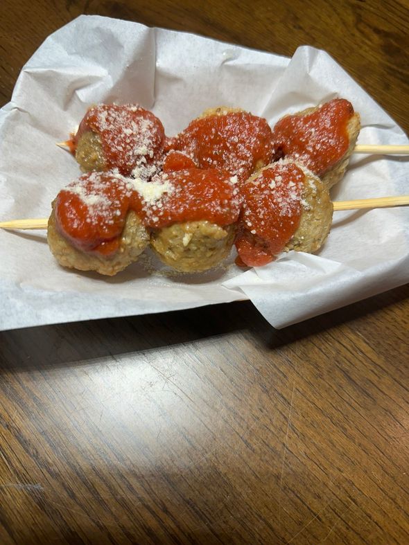Skewered fried dough balls topped with red sauce and powdered sugar on a paper-lined tray