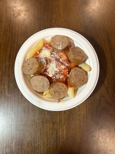 White bowl of meatballs with tomato sauce and grated cheese on a wooden table.