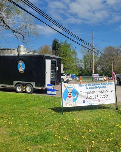 Food truck with banner parked on grassy roadside under blue sky