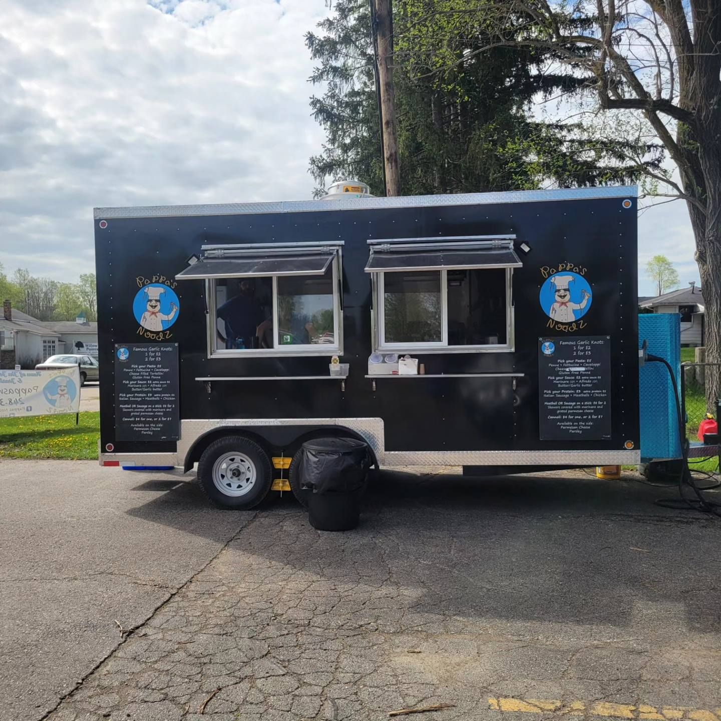Black food truck with serving windows and menu signs parked on a paved lot outdoors
