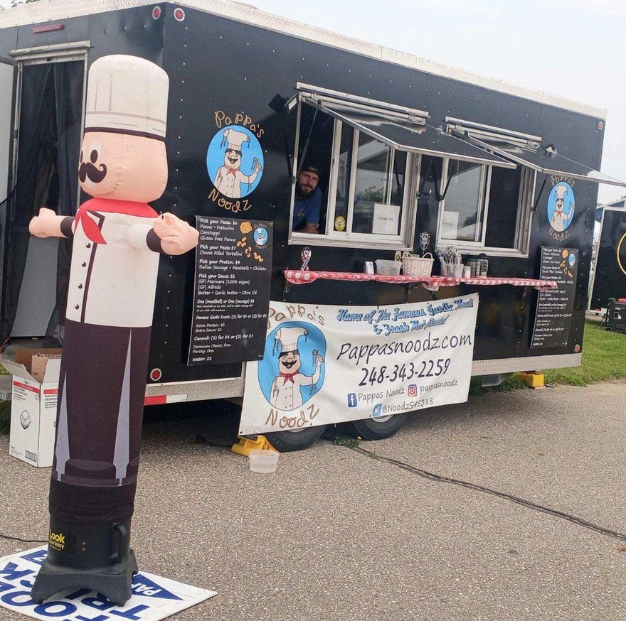 Food truck with a chef mascot figure and service window, black exterior with menu signs and banner.