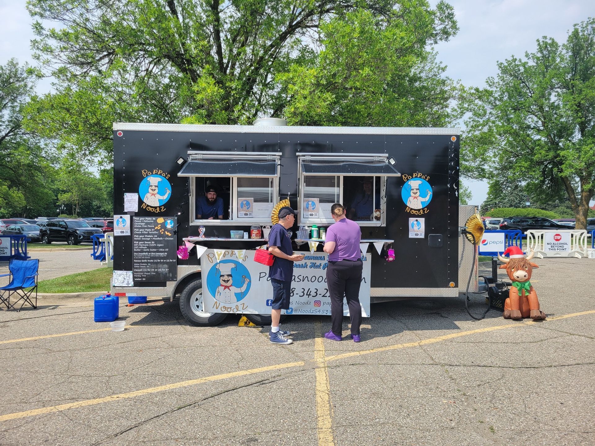 Black food truck at an outdoor event with people ordering at the service windows.