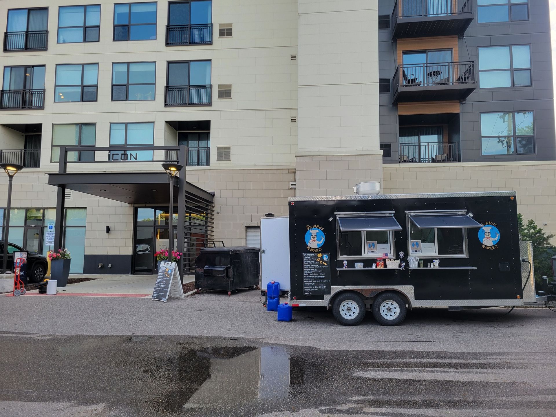 Food truck parked beside an apartment building on a wet street, with people standing nearby.