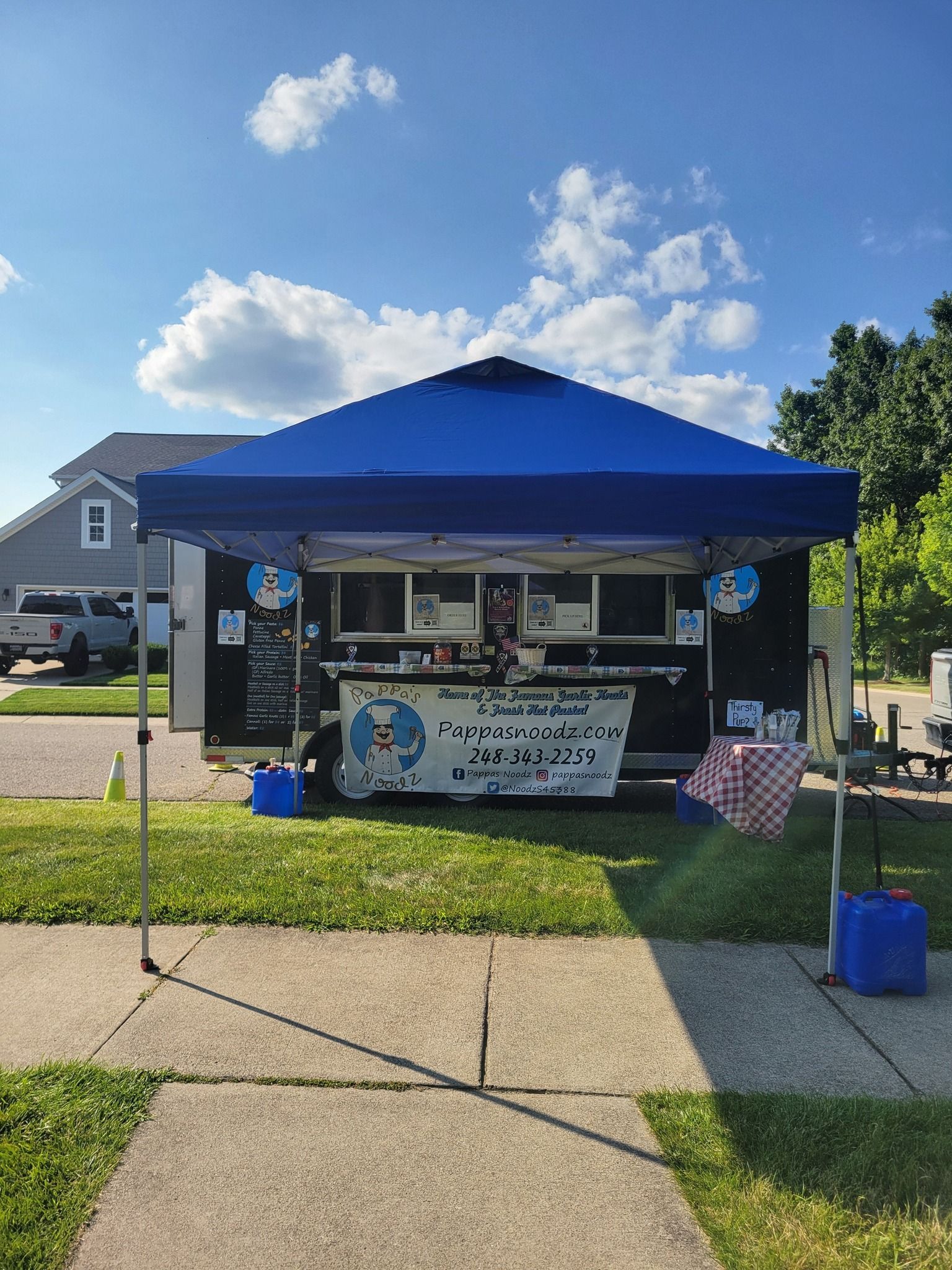 Blue canopy food booth outdoors with banner, tables, and coolers on a sunny sidewalk