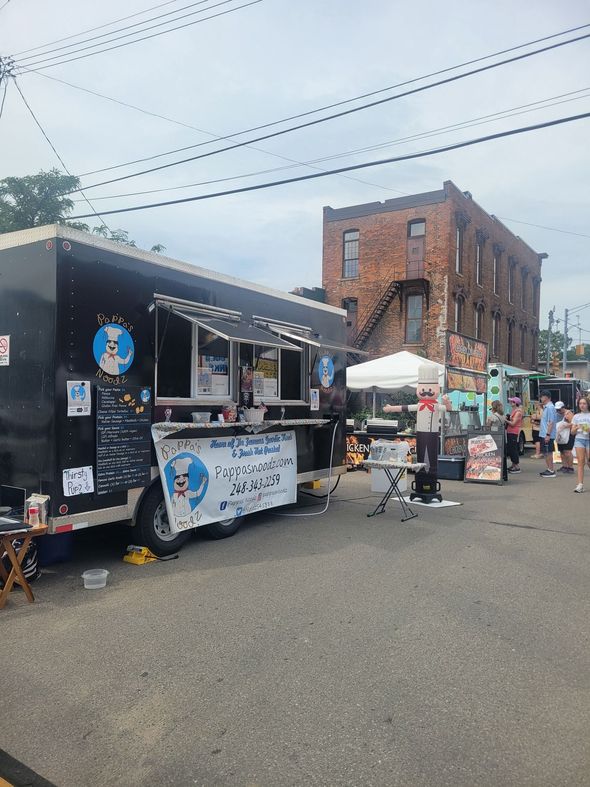 Street food market with food trucks and pedestrians beside brick buildings under cloudy sky
