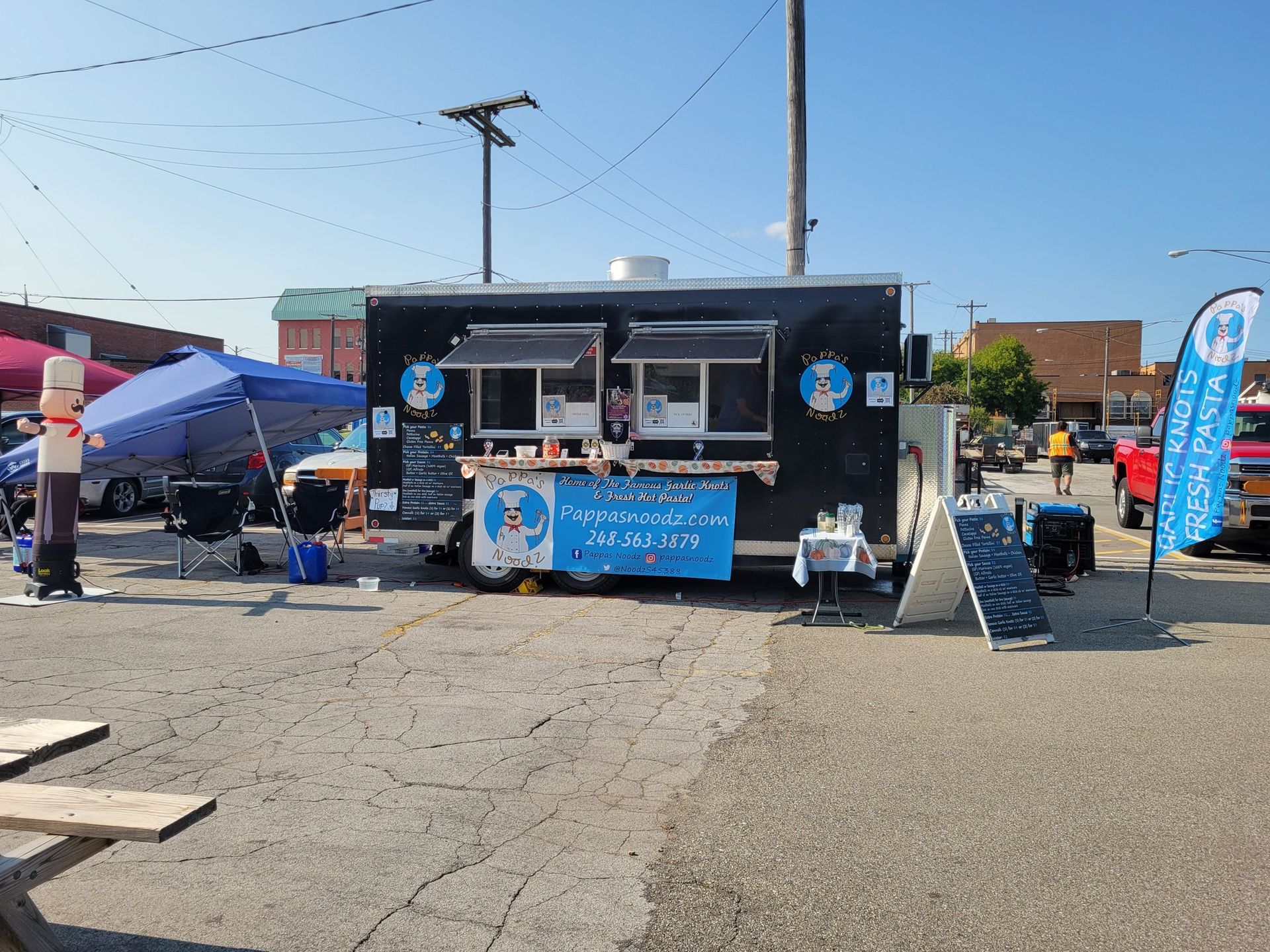 Food truck at an outdoor event with a blue banner, tents, and people under a clear sky.