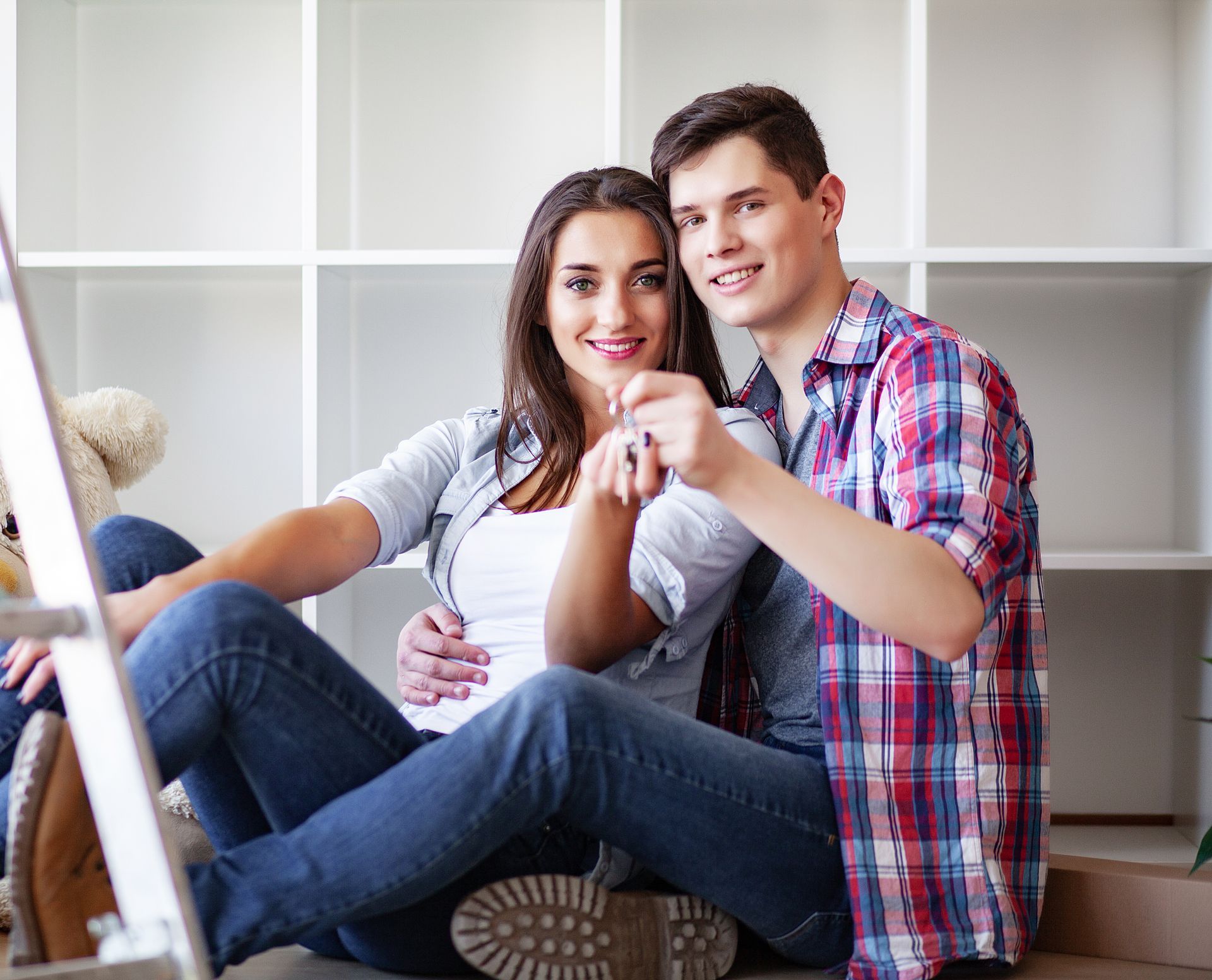 A man and a woman are sitting on the floor holding keys to their new home.