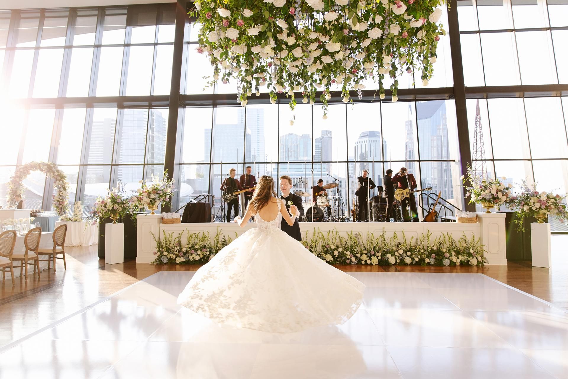 Bride and groom dancing at a wedding reception with a band in front of a cityscape.