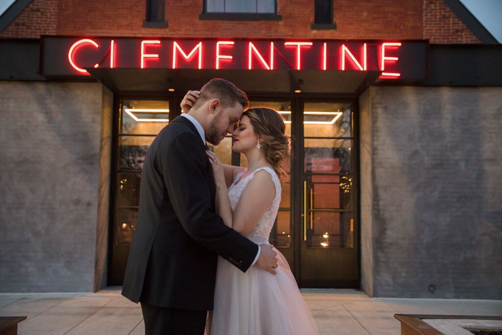 Bride and groom are kissing in front of a building with a neon sign by Wedding Planner Nashville