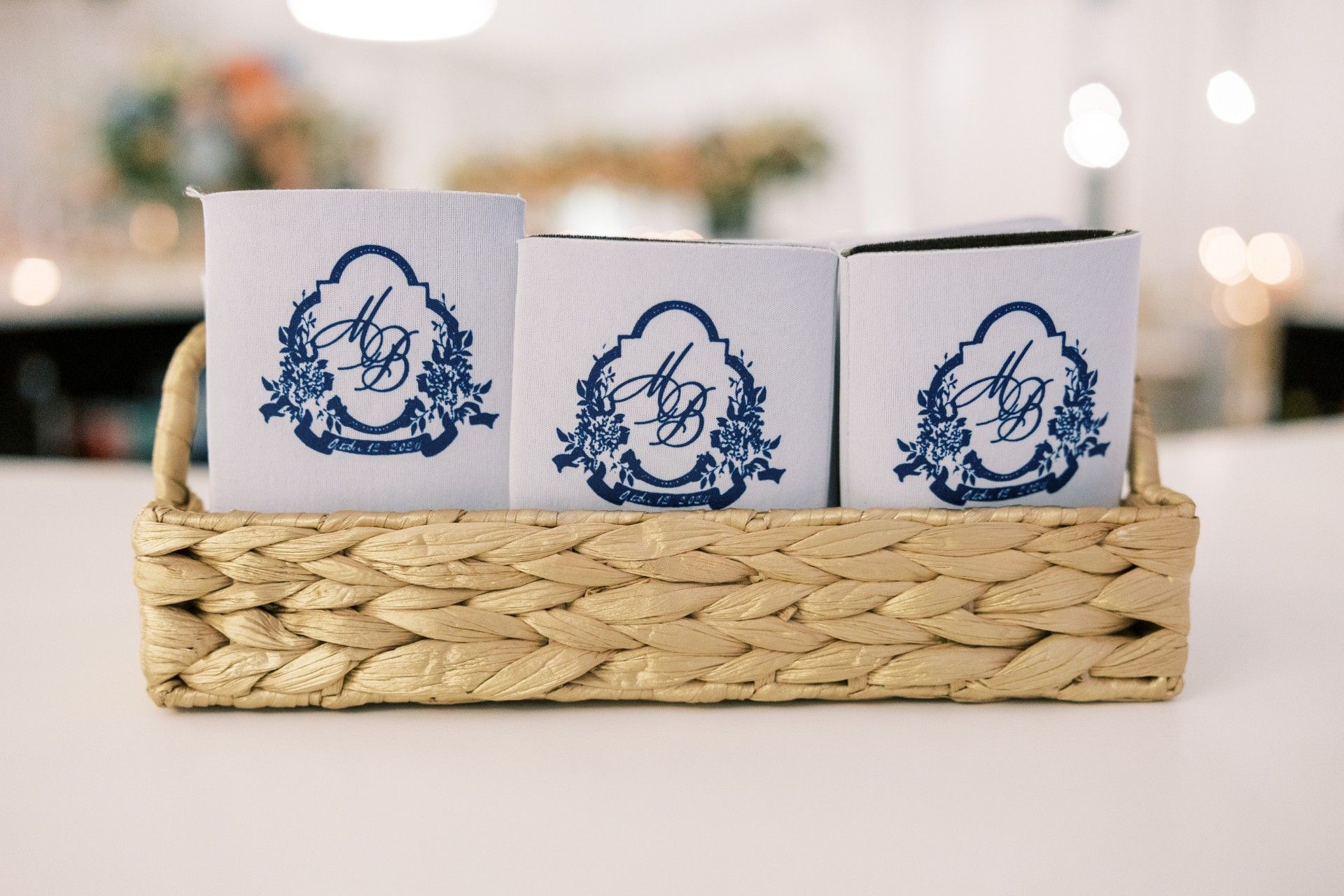 Three blue and white monogrammed can coolers are in a wicker basket by Luxury Wedding Planners in Nashville, TN
