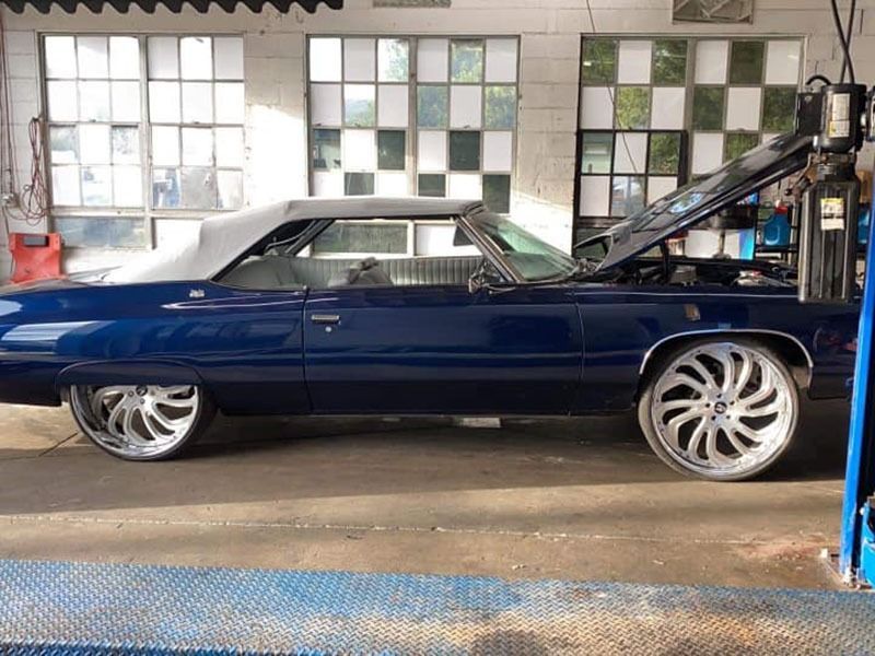Blue classic car in a garage, raised hood, with large chrome rims.